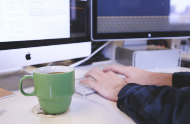 Person typing at a computer. A green mug sits next to their left hand.