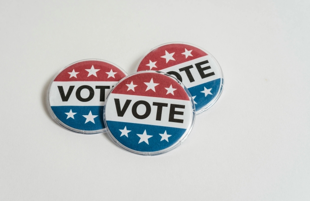 Three red, white, and blue VOTE pins on a blank background
